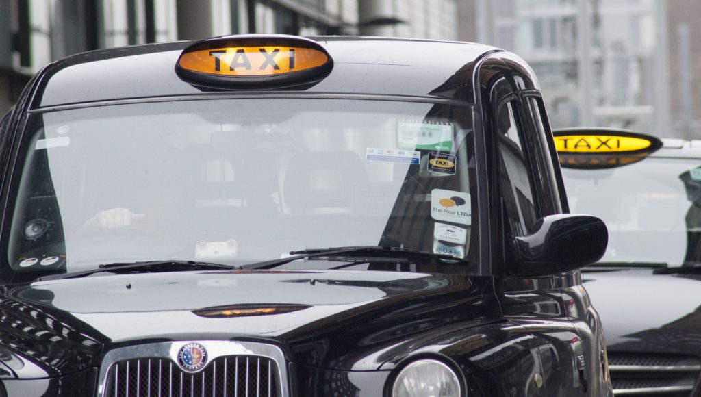 A queue of black cabs waiting at a rank, with orange 'taxi' lights on